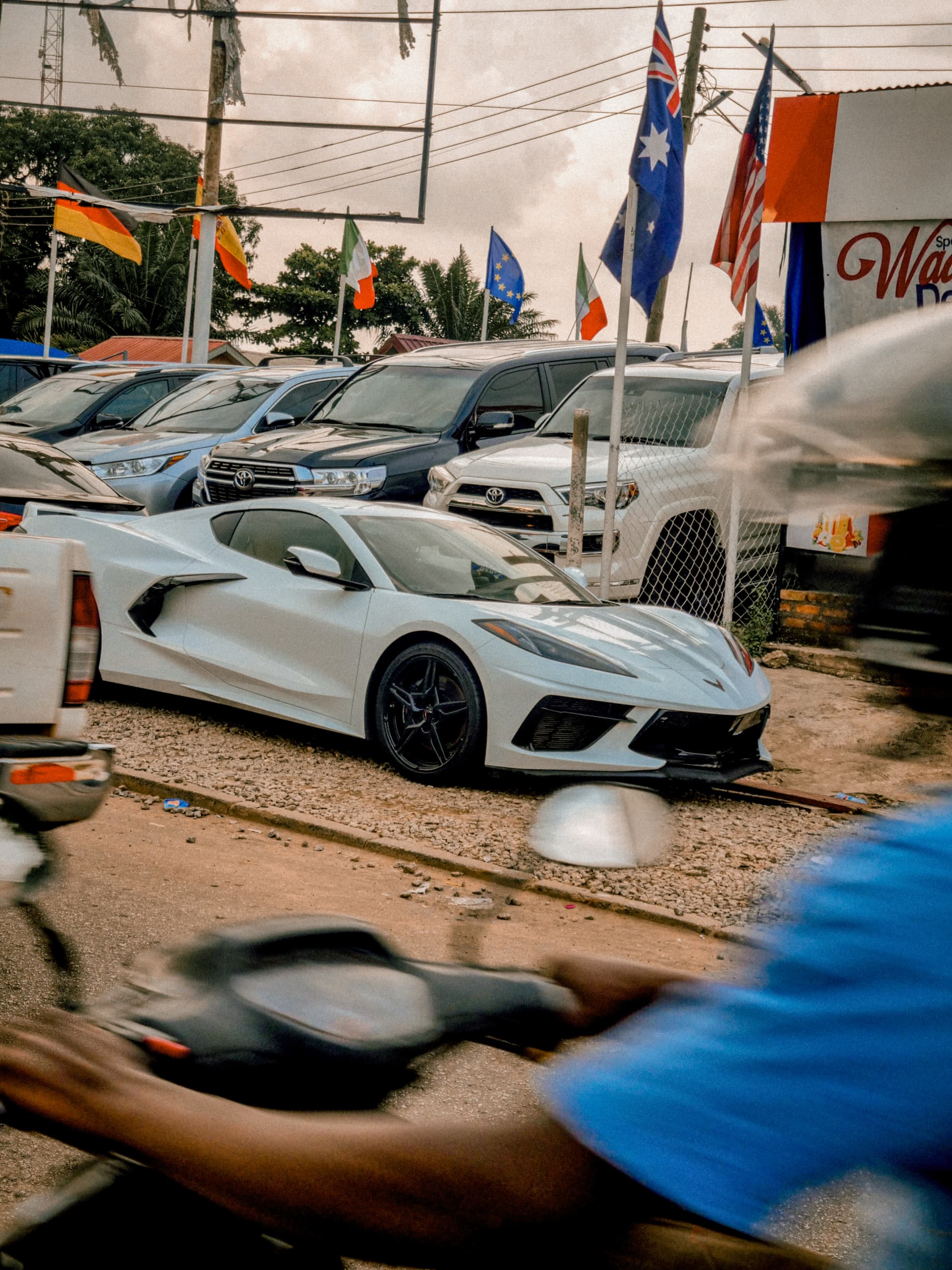 White Corvette parked at a car dealership with national flags