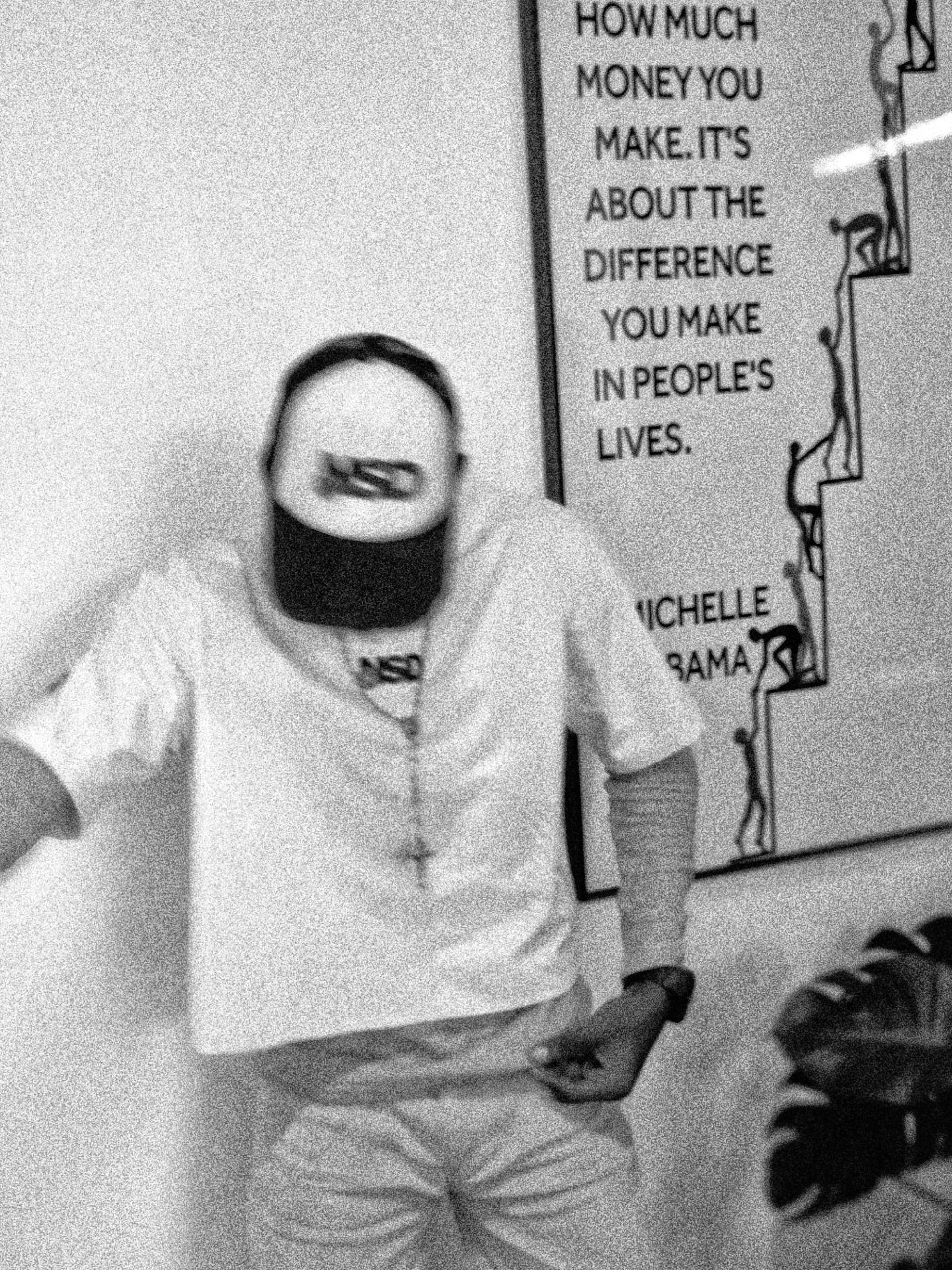 Black and white portrait of a person wearing a cap, leaning near a quote poster